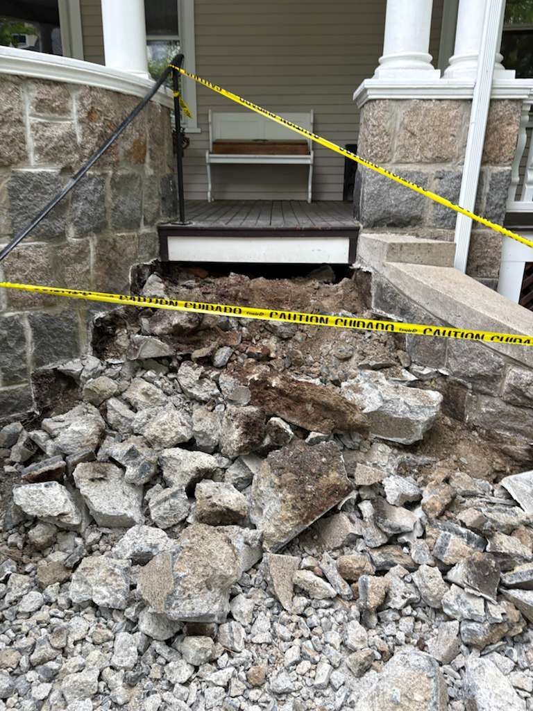Stone steps undergoing repair; rubble and caution tape surround the entrance to a porch.