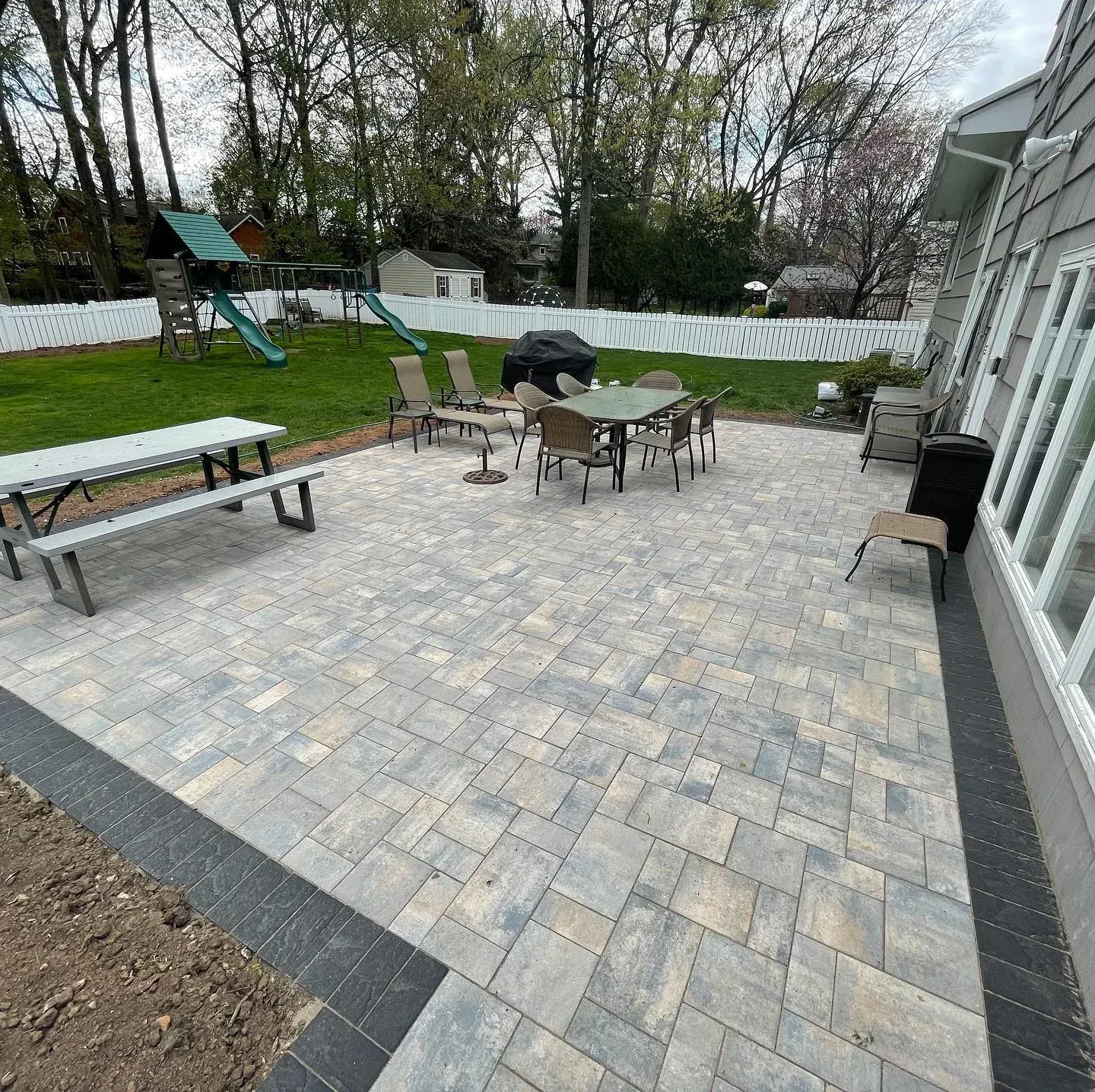 Patio with paving stones, dining set, and picnic table; backyard with playset.