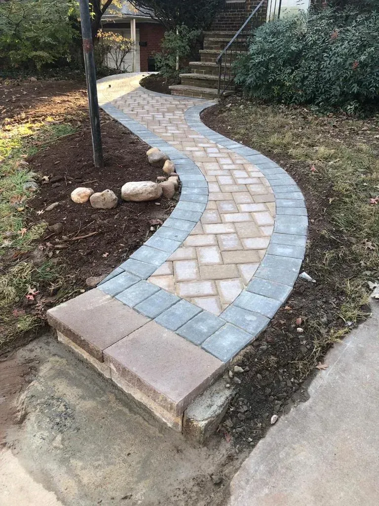 A winding brick pathway with three colors leads to a house with steps.