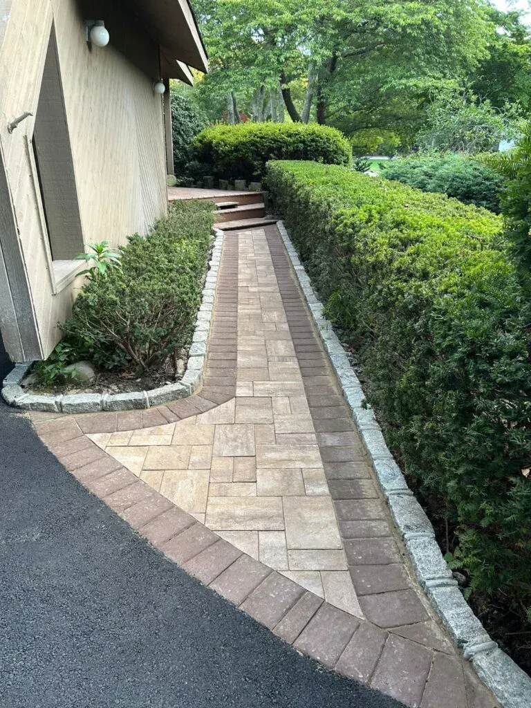 Pathway with brick pavers and a hedge leading to a set of stairs.