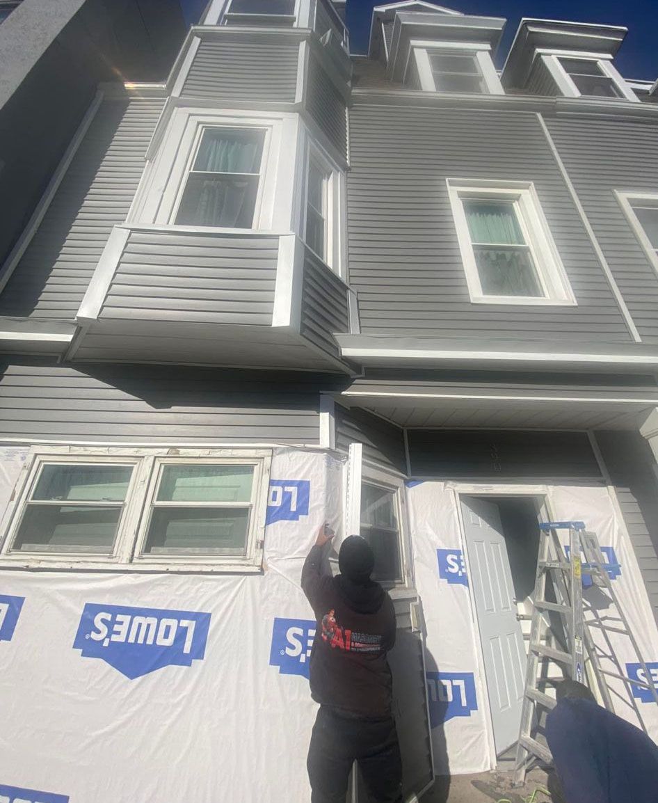 Person installing siding on a multi-story building. Grey siding, white windows, and Lowe's wrap.