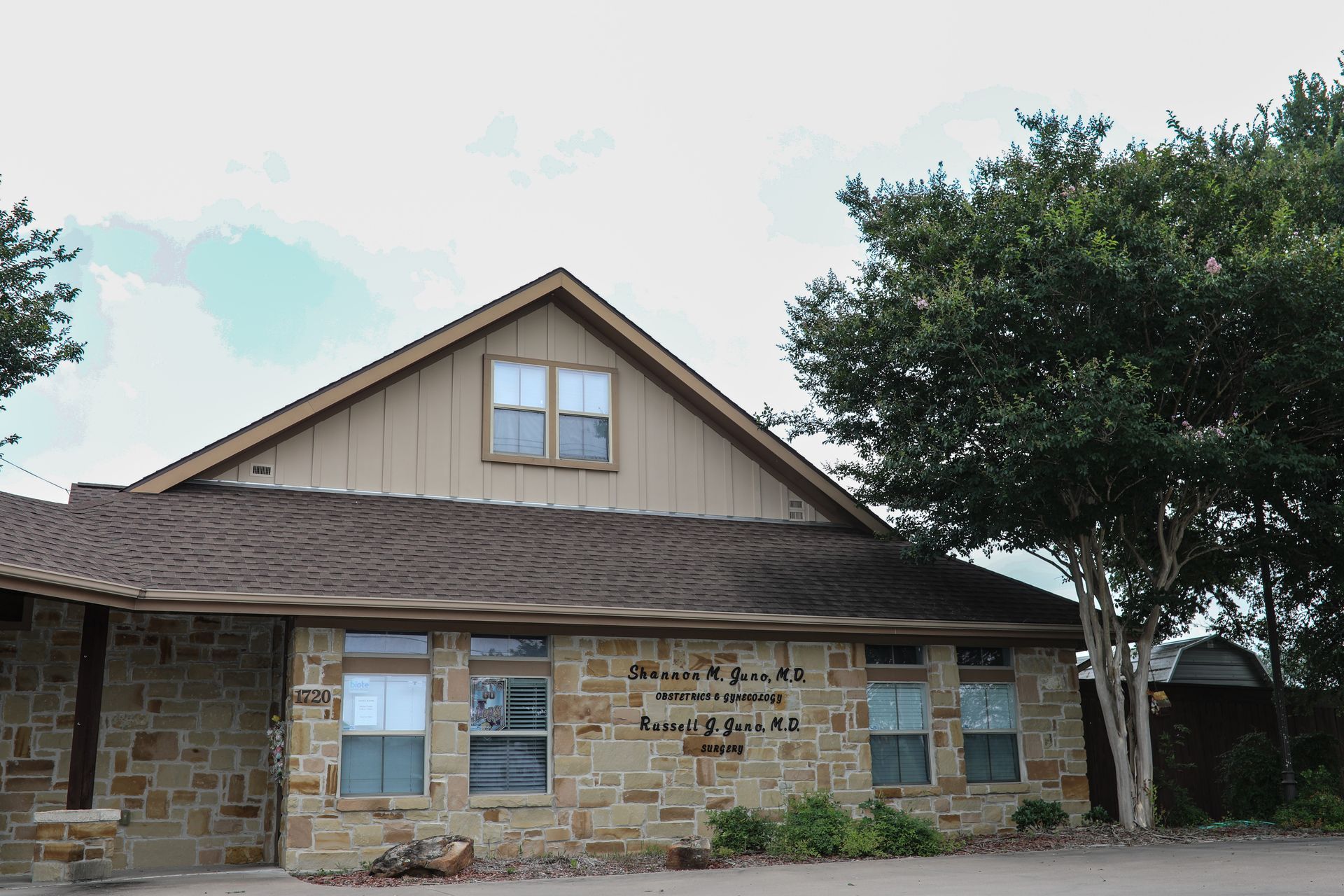 A stone building with a brown roof and a tree in front of it