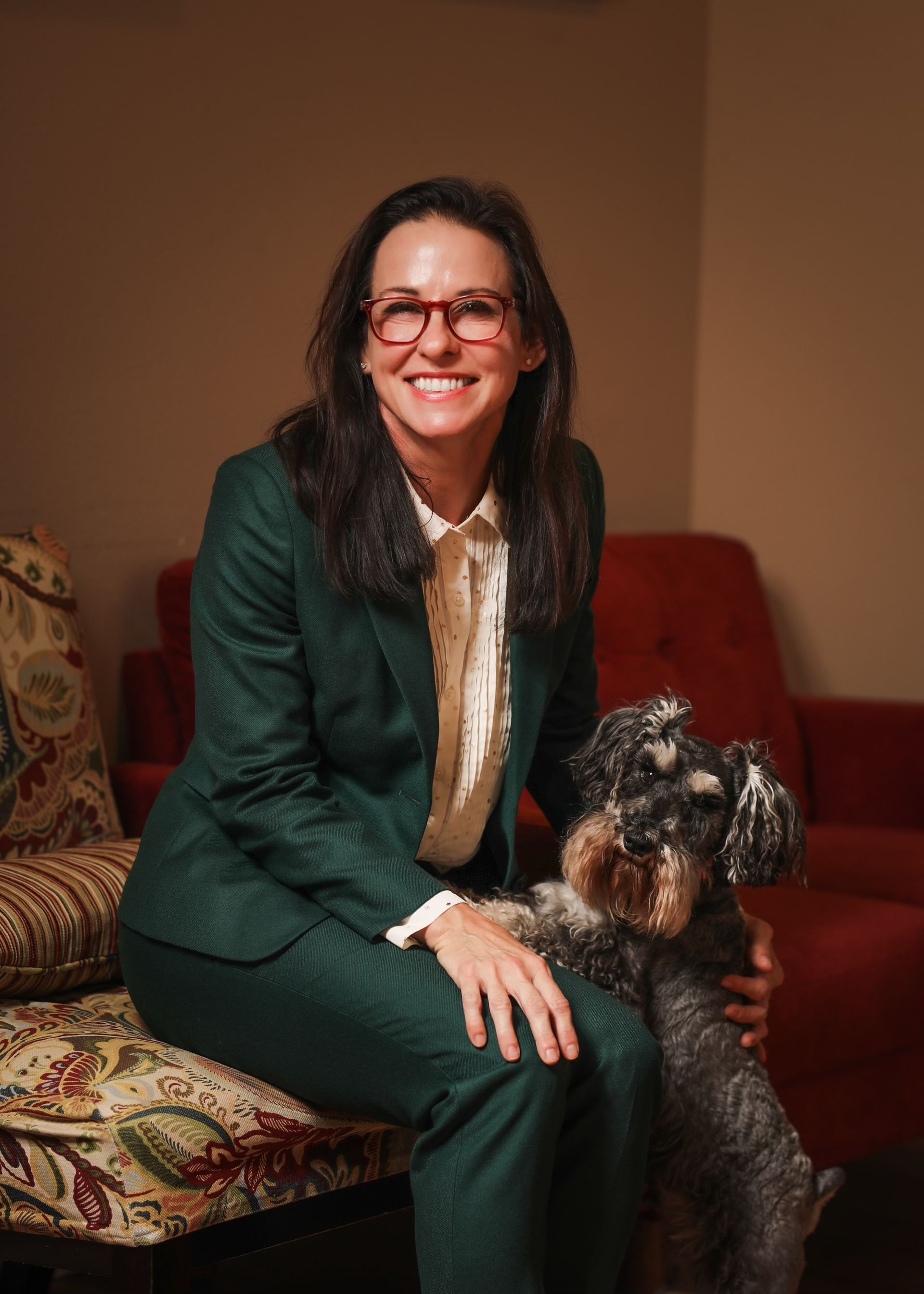 A woman in a suit is sitting on a chair with a dog.