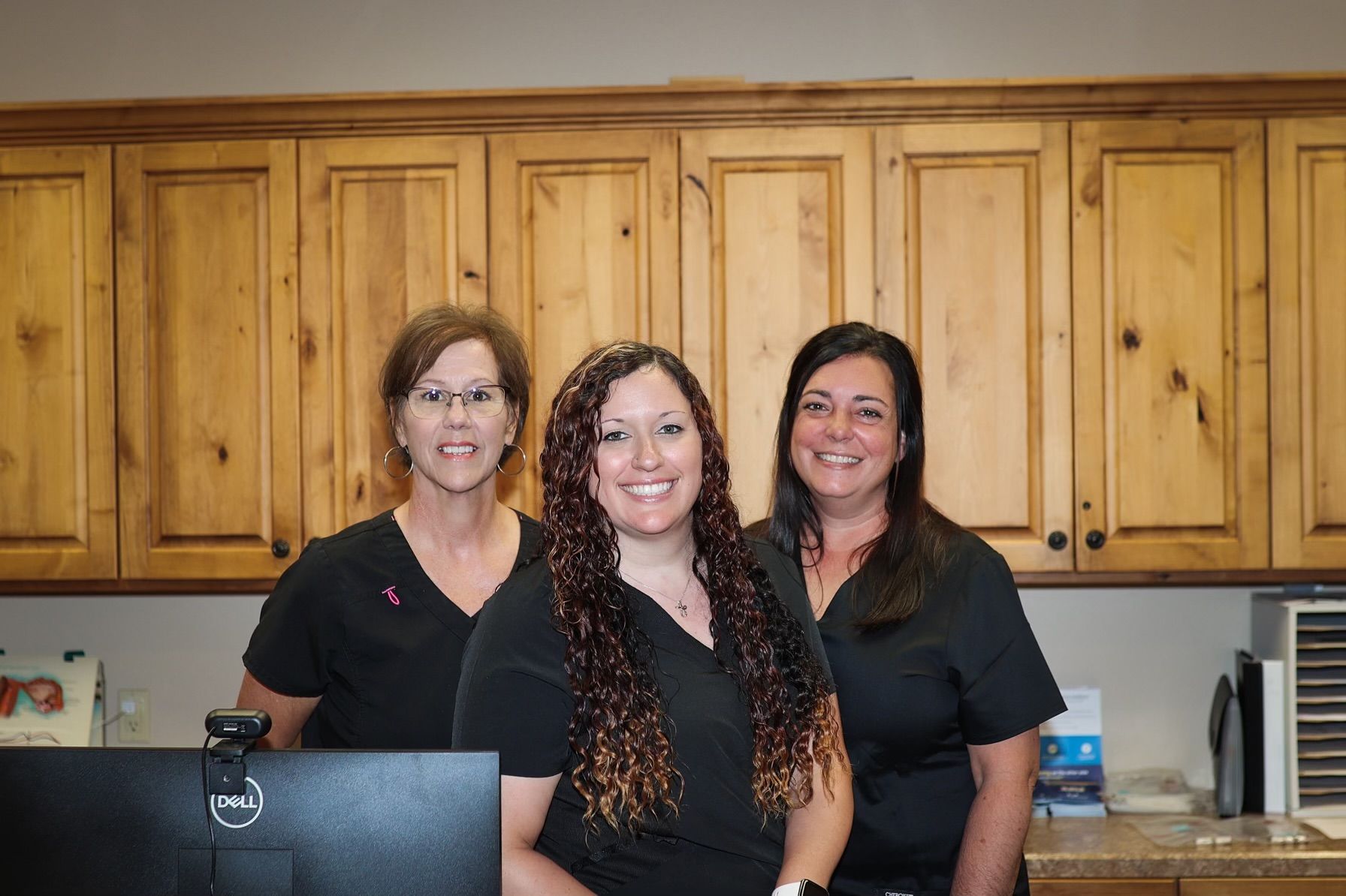 Three women are posing for a picture in front of a computer in a kitchen.
