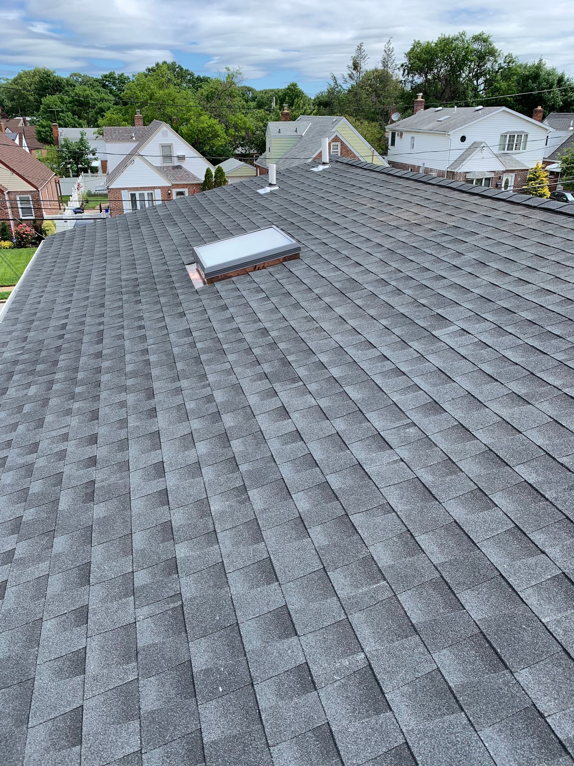 Gray shingle roof with skylight in suburban neighborhood, overcast sky in background.