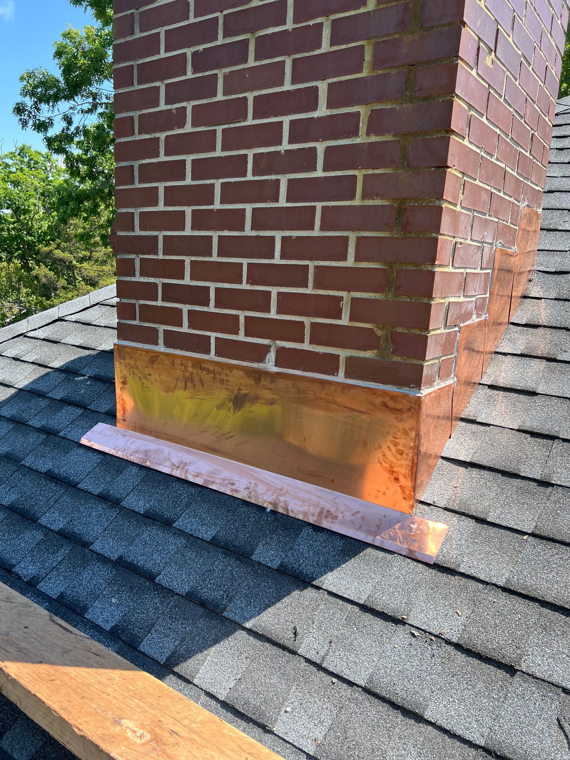 Brick chimney with copper flashing on a shingled roof.
