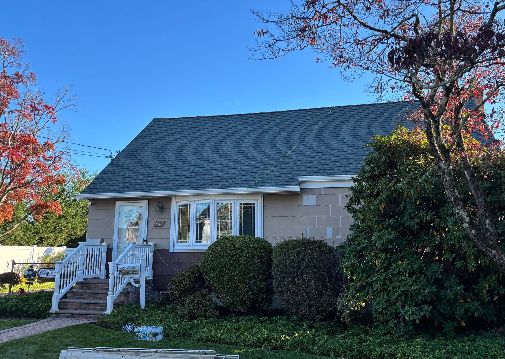 Tan house with green roof, white window frame, and small front porch. Autumn foliage on trees.