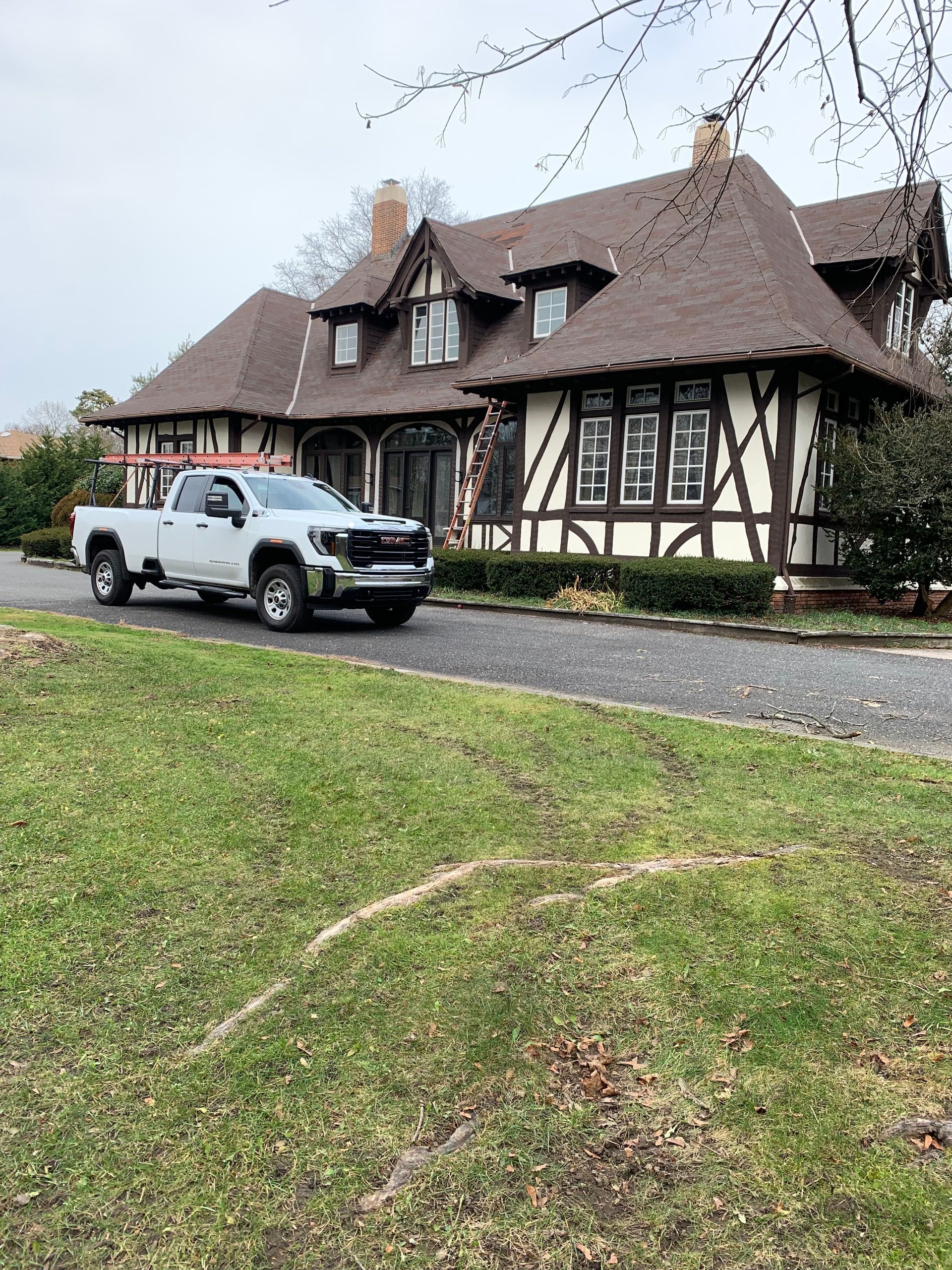 White pickup truck parked in front of a Tudor-style house with brown and white exterior on a cloudy day.