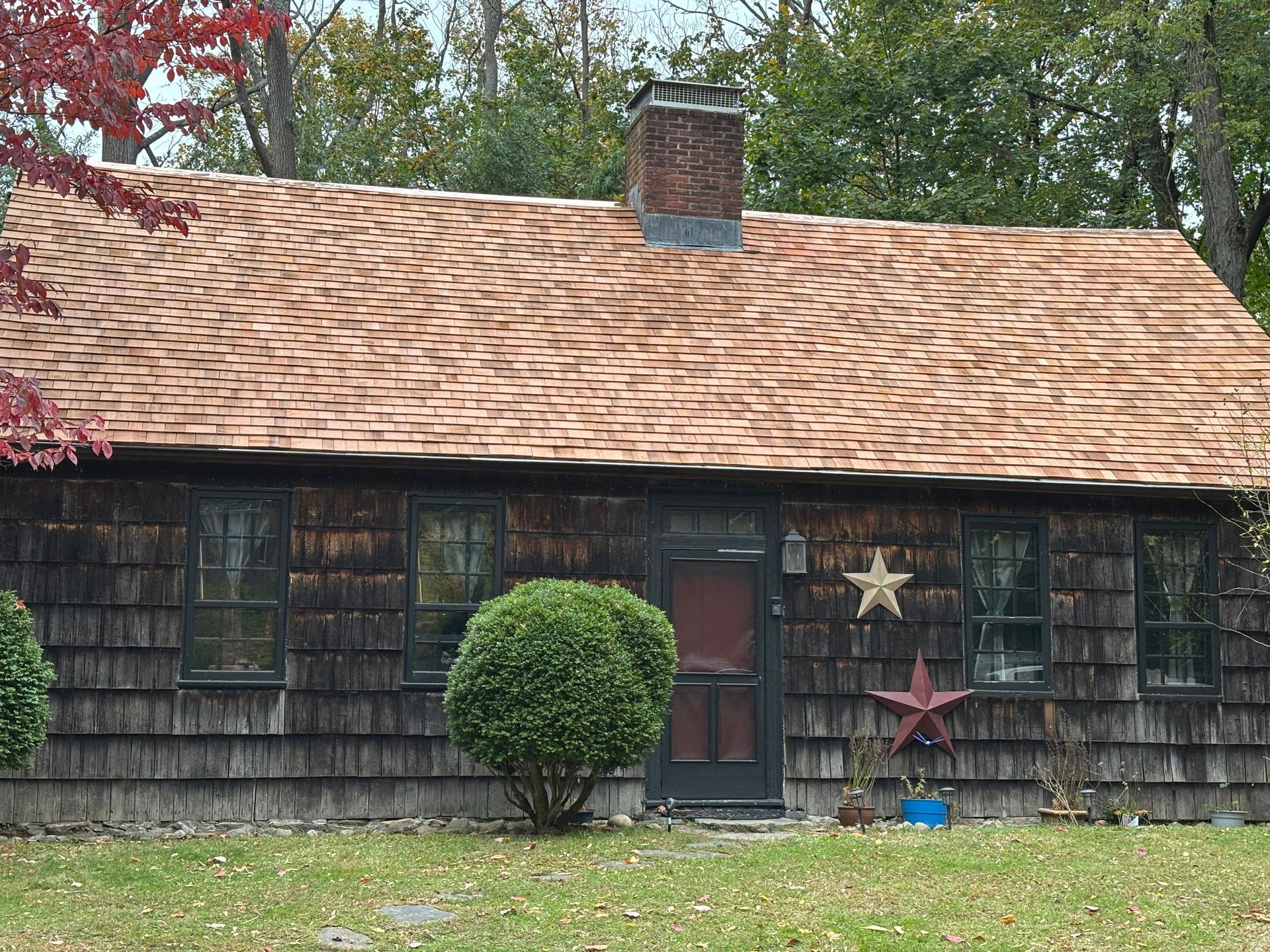 Cottage with shingle siding, weathered roof, brick chimney, and decorative stars on the door.