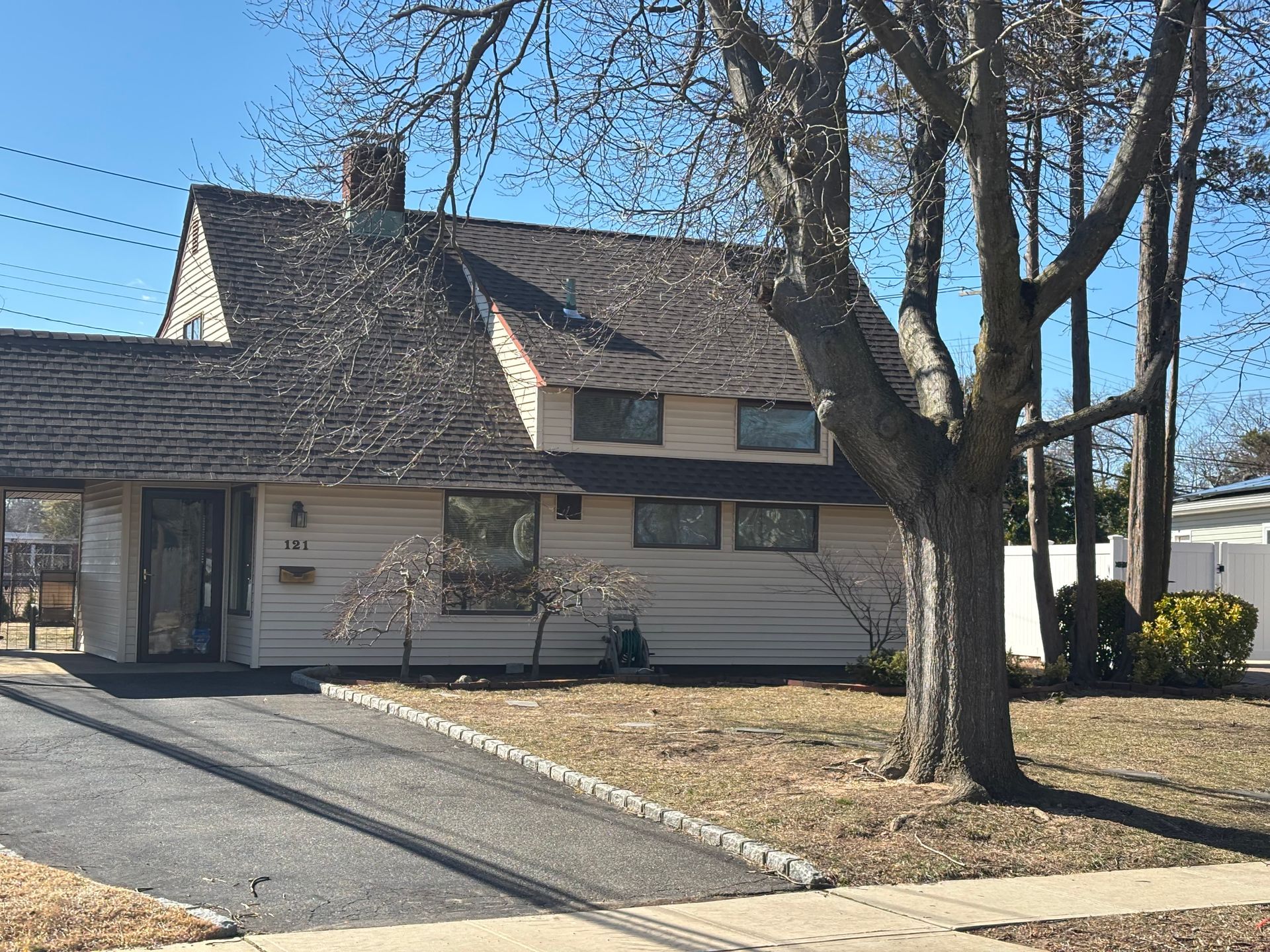 House with dark roof, carport, and asphalt driveway on a sunny day.