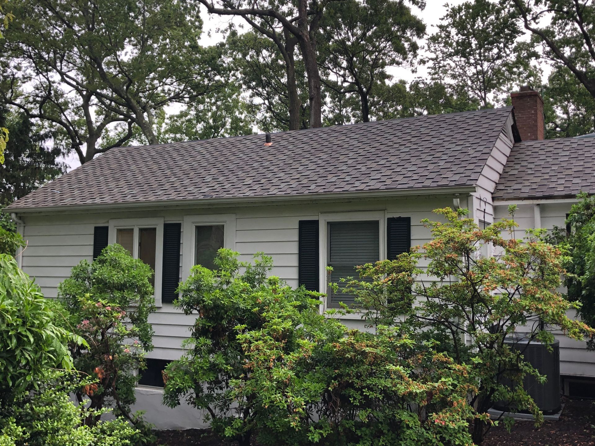 White house with severely damaged roof, surrounded by green trees.