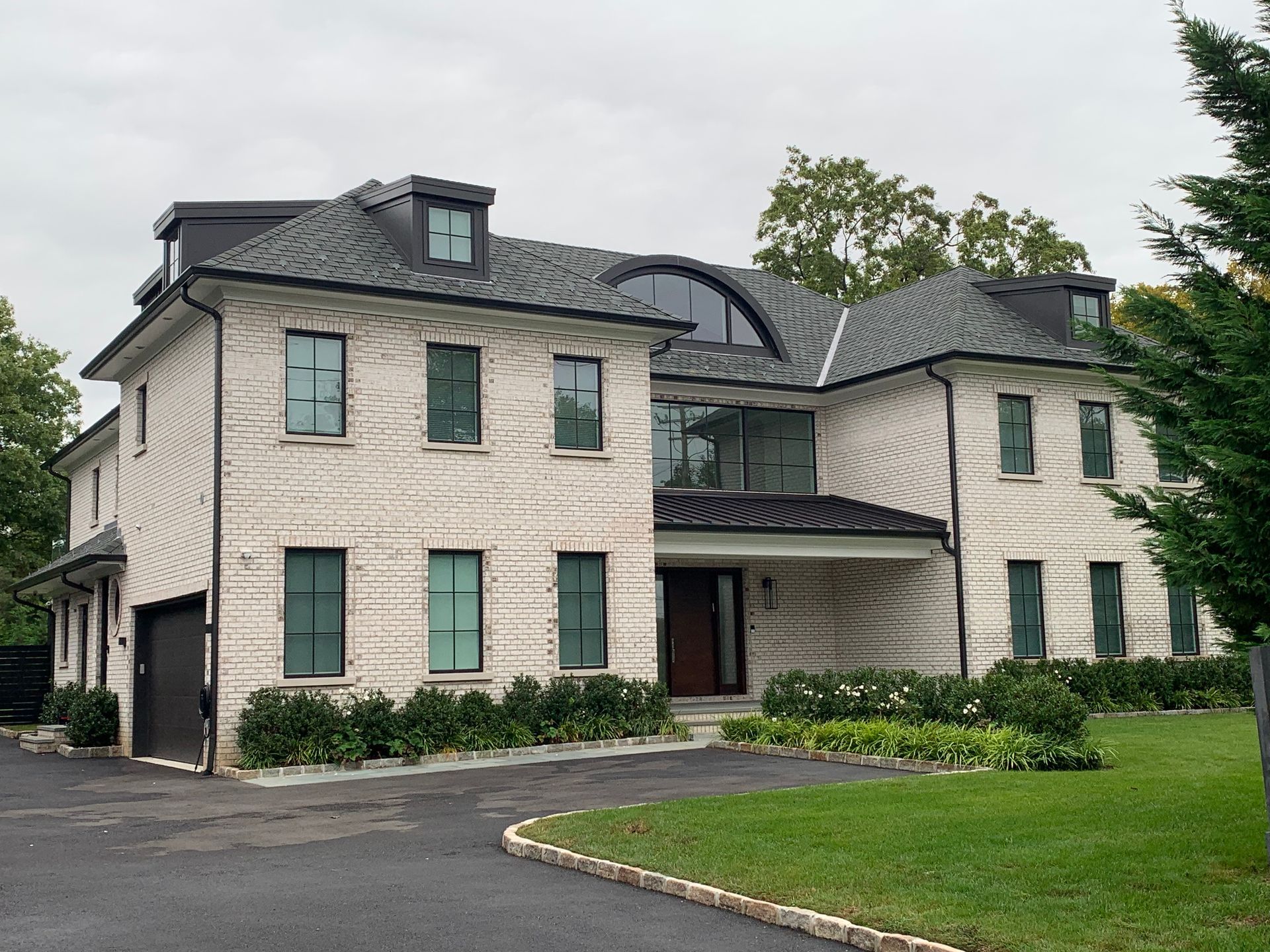 Two-story brick house with dark roof and trim, arched window, and front lawn.