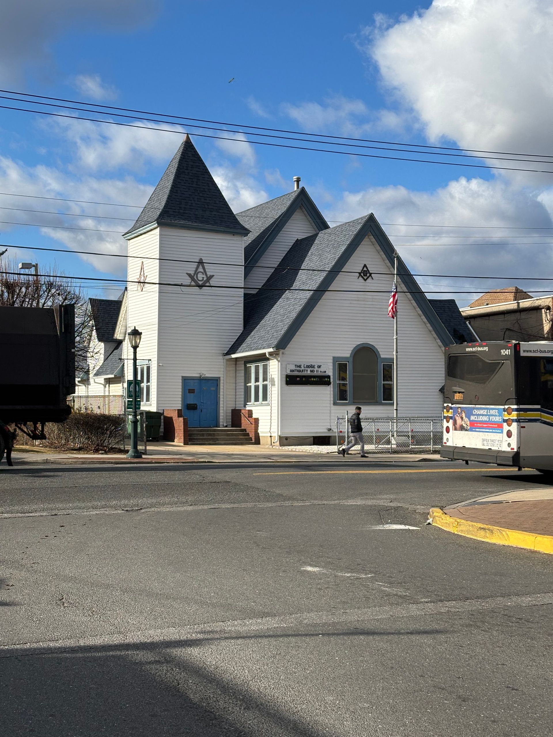 White Masonic lodge building with blue door, gray roof, flag on pole, street view.