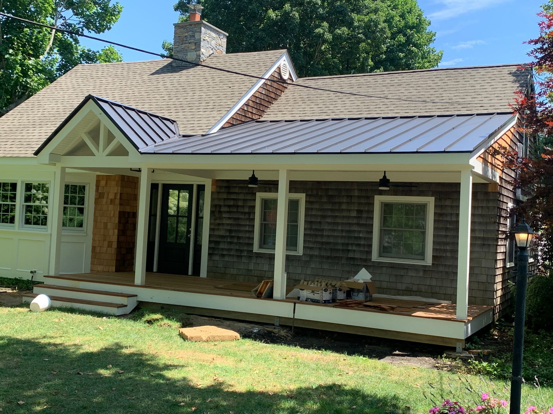 Small house with a new dark metal roof porch and wooden siding, surrounded by grass and trees.