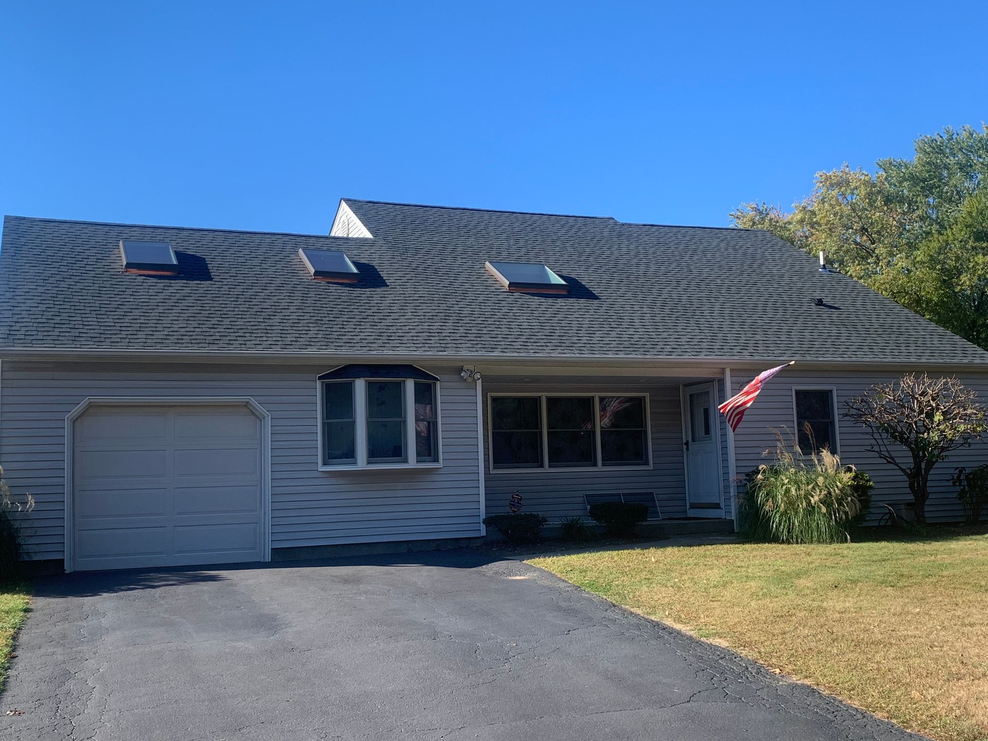 Ranch-style house with gray siding, garage, and dark roof with three skylights, under a blue sky.