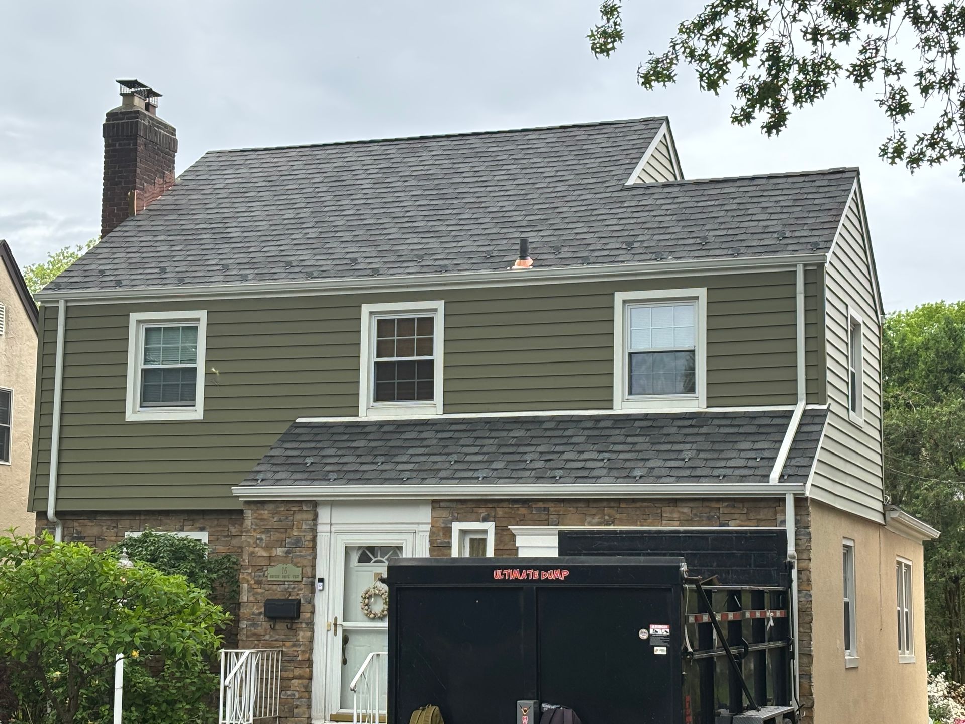 Two-story house with green siding, a gray roof, and a brick base.