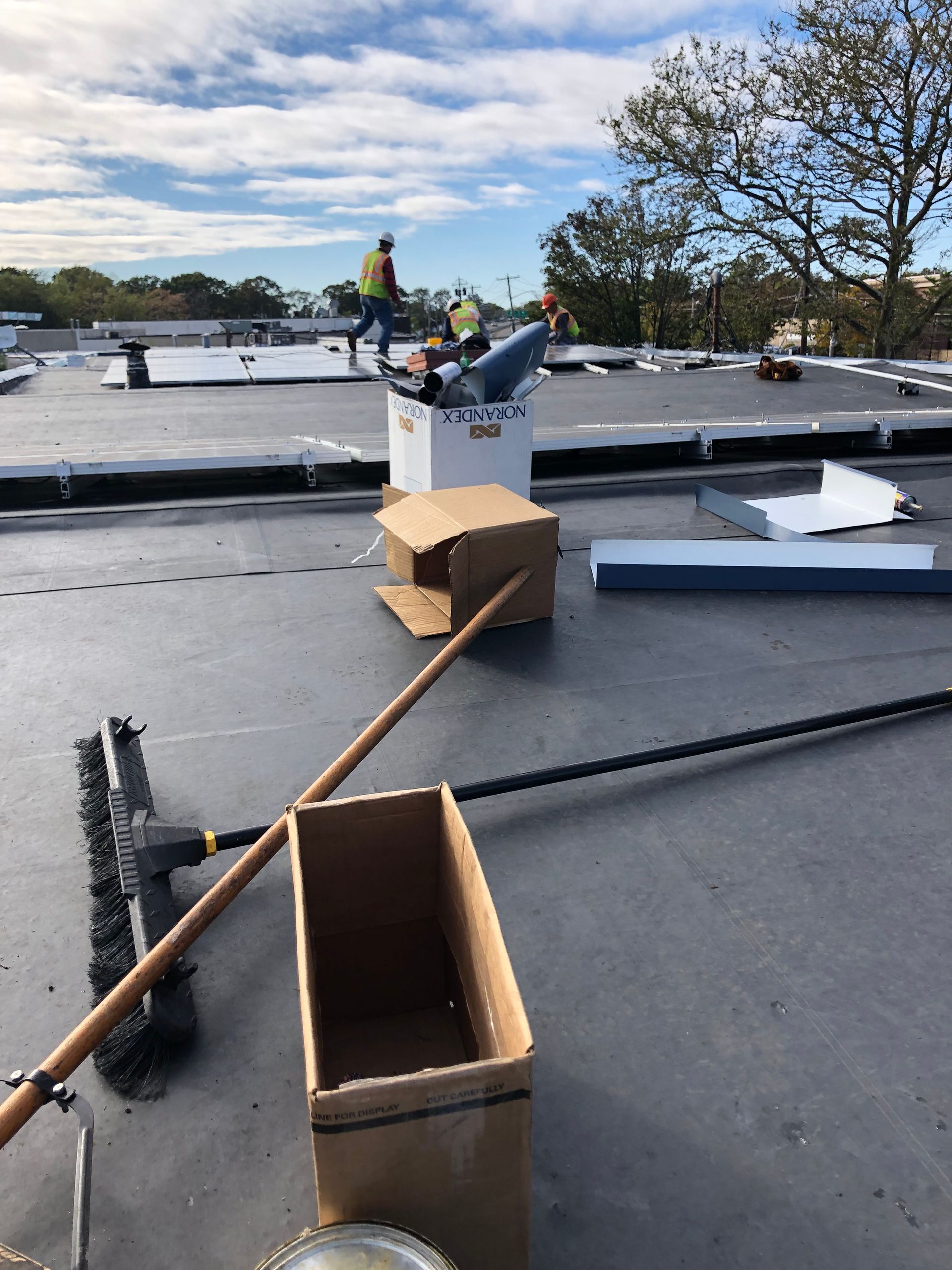 Workers on a flat roof with tools and supplies under a cloudy sky.