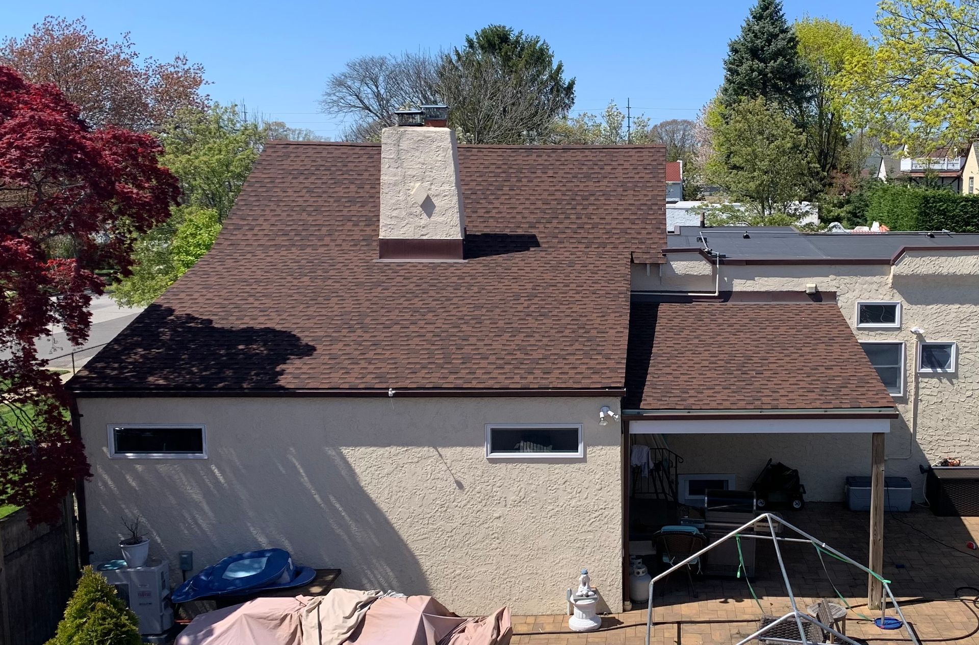 Brown shingled roof on a stucco house with a chimney. Patio with outdoor furniture to the right.