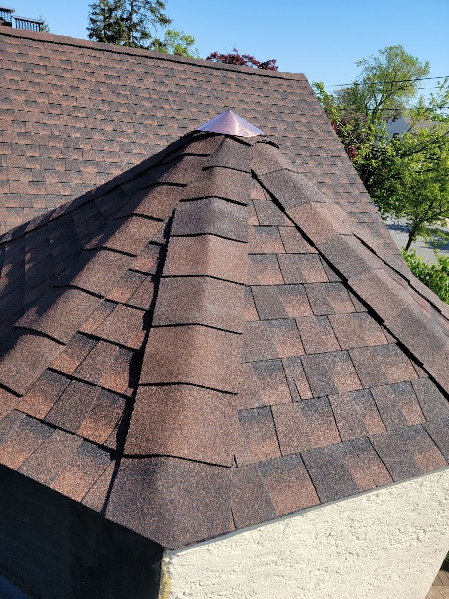 Brown shingled roof with a copper cap, viewed from an upward angle under a clear sky.