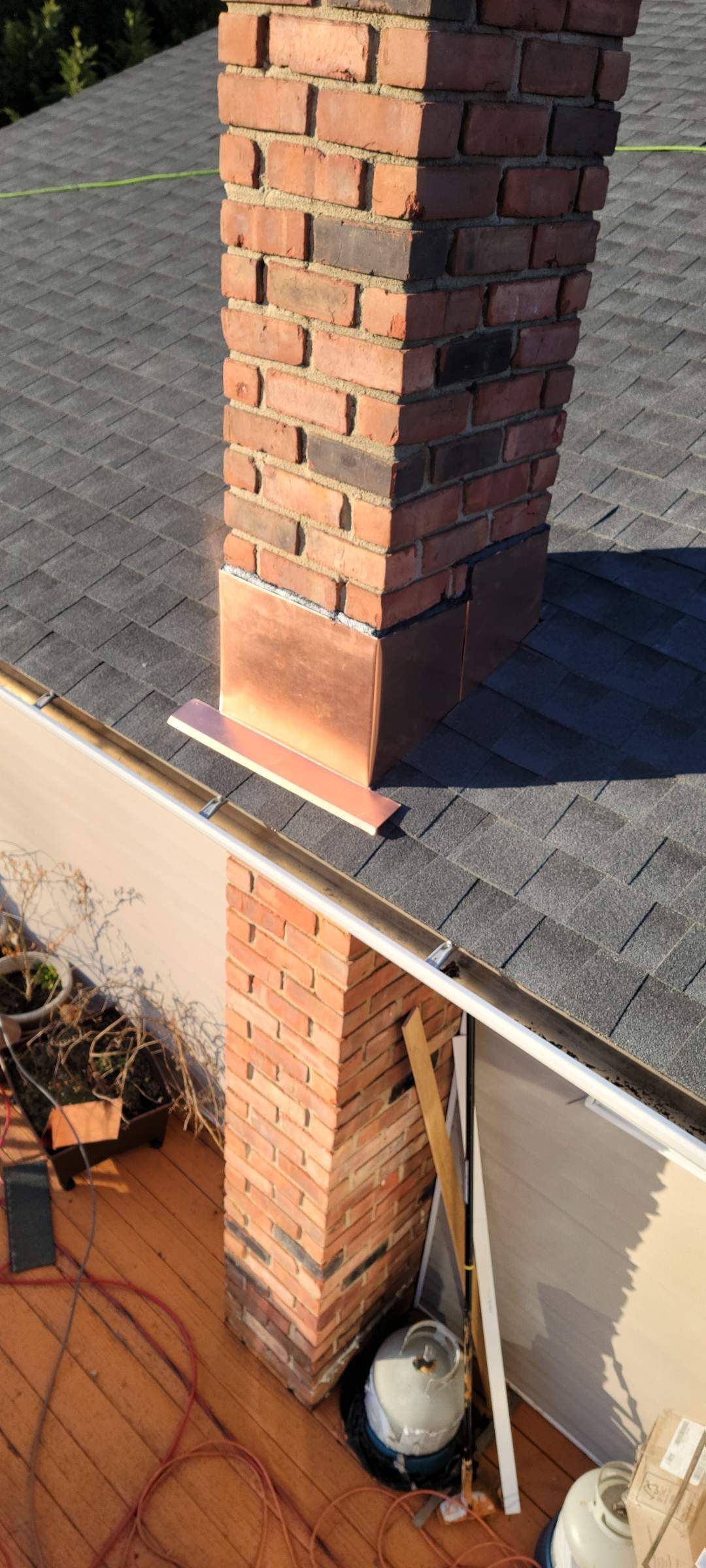 Brick chimney on a dark shingled roof with copper flashing. Ground level view of the same chimney.