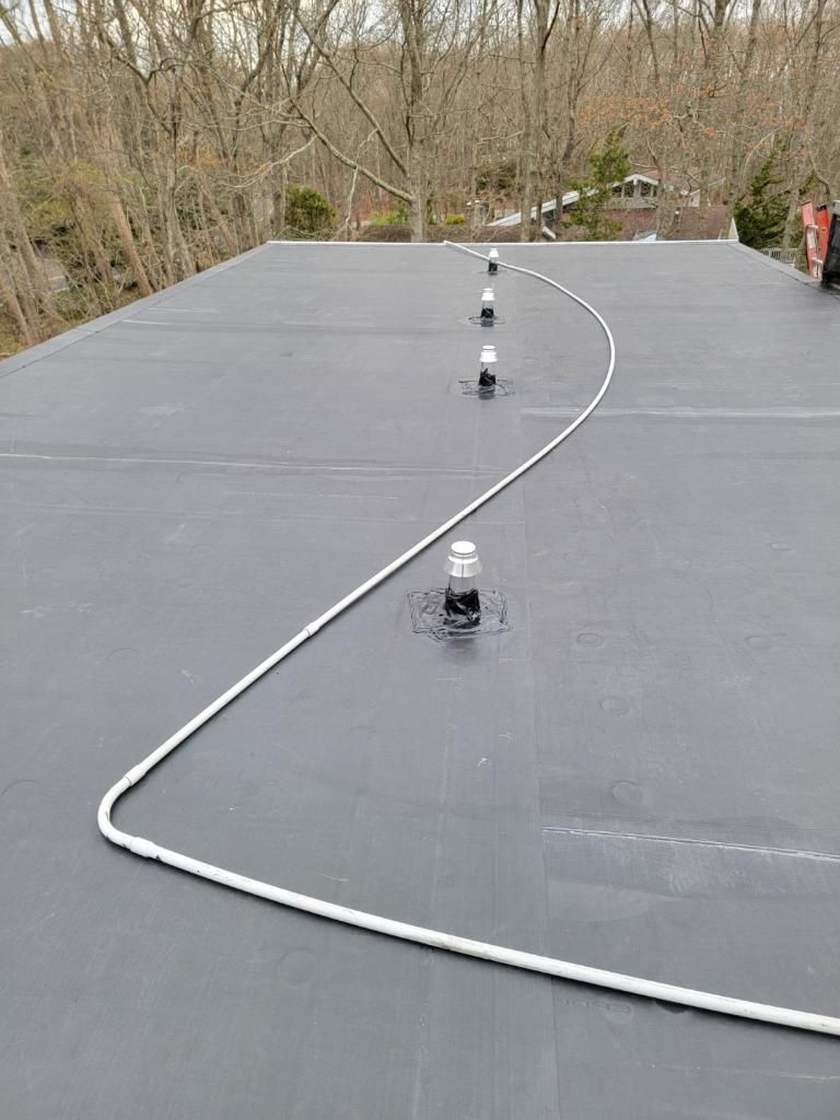 Flat, black rooftop with white rope snaking around vertical pipes. Trees in the background.