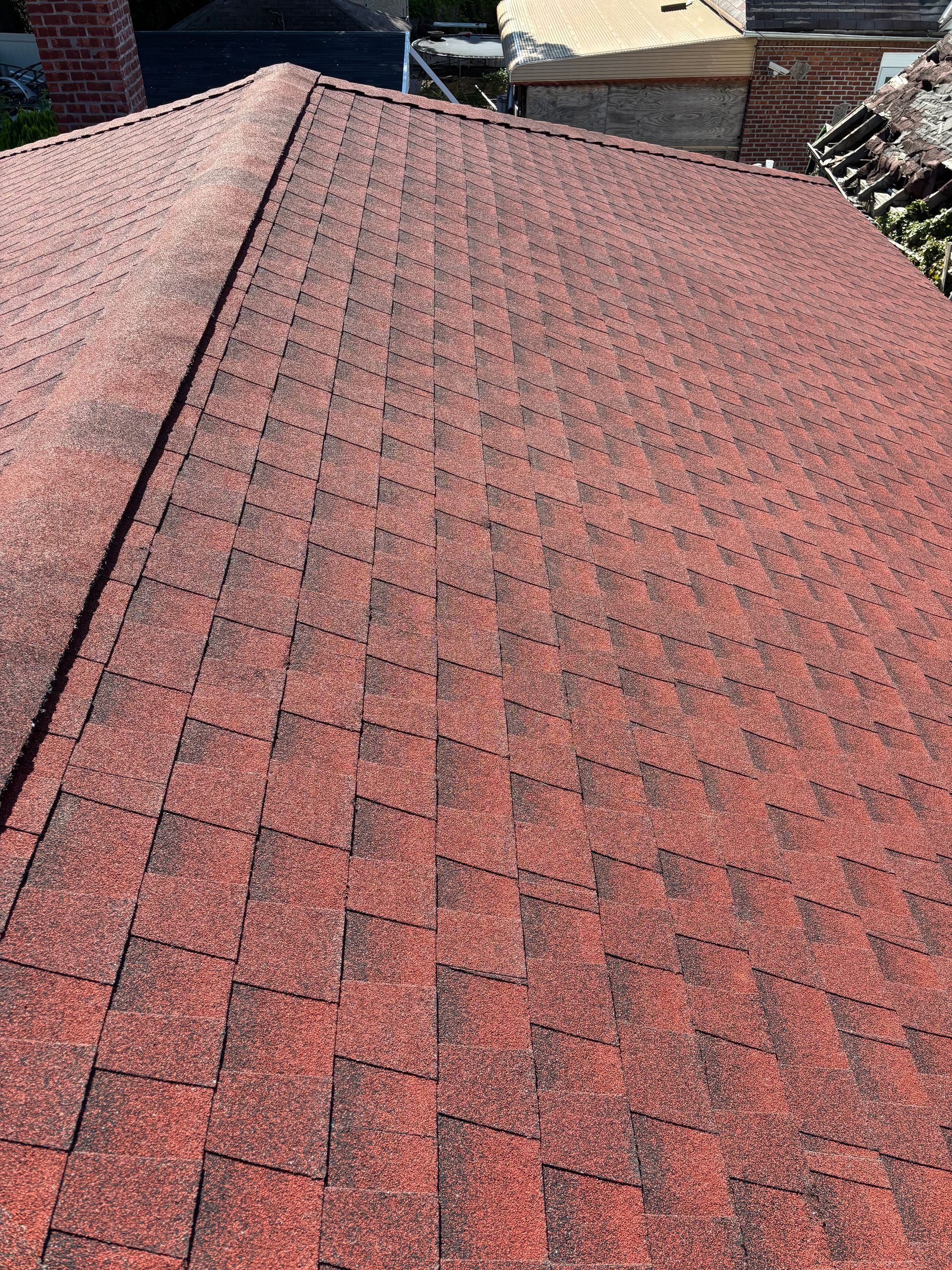 Red asphalt shingle roof, angled view, outdoor setting, with a prominent ridge line and brick chimney.