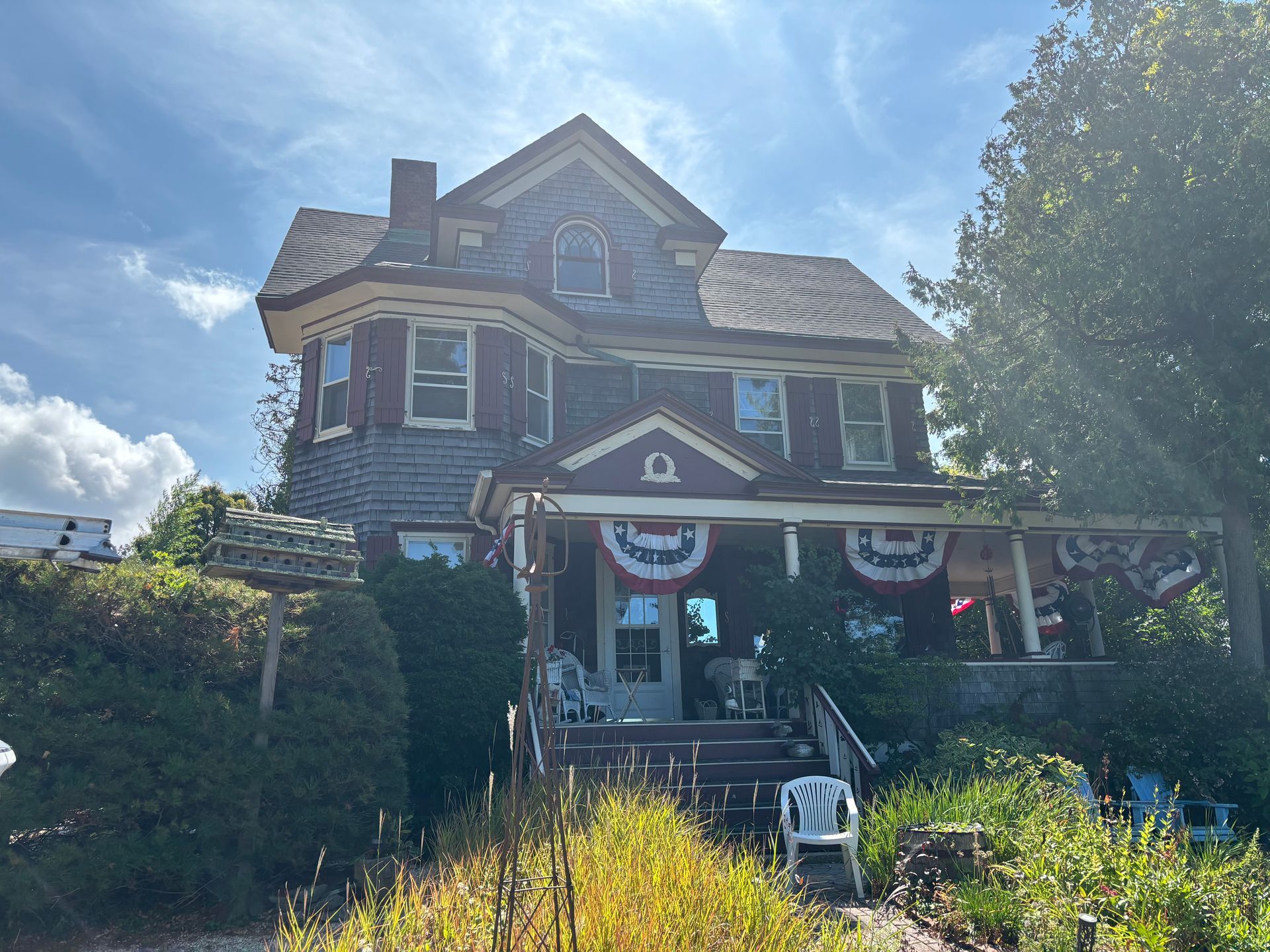 Victorian-style house with red trim, gray siding, and a porch decorated with patriotic bunting.