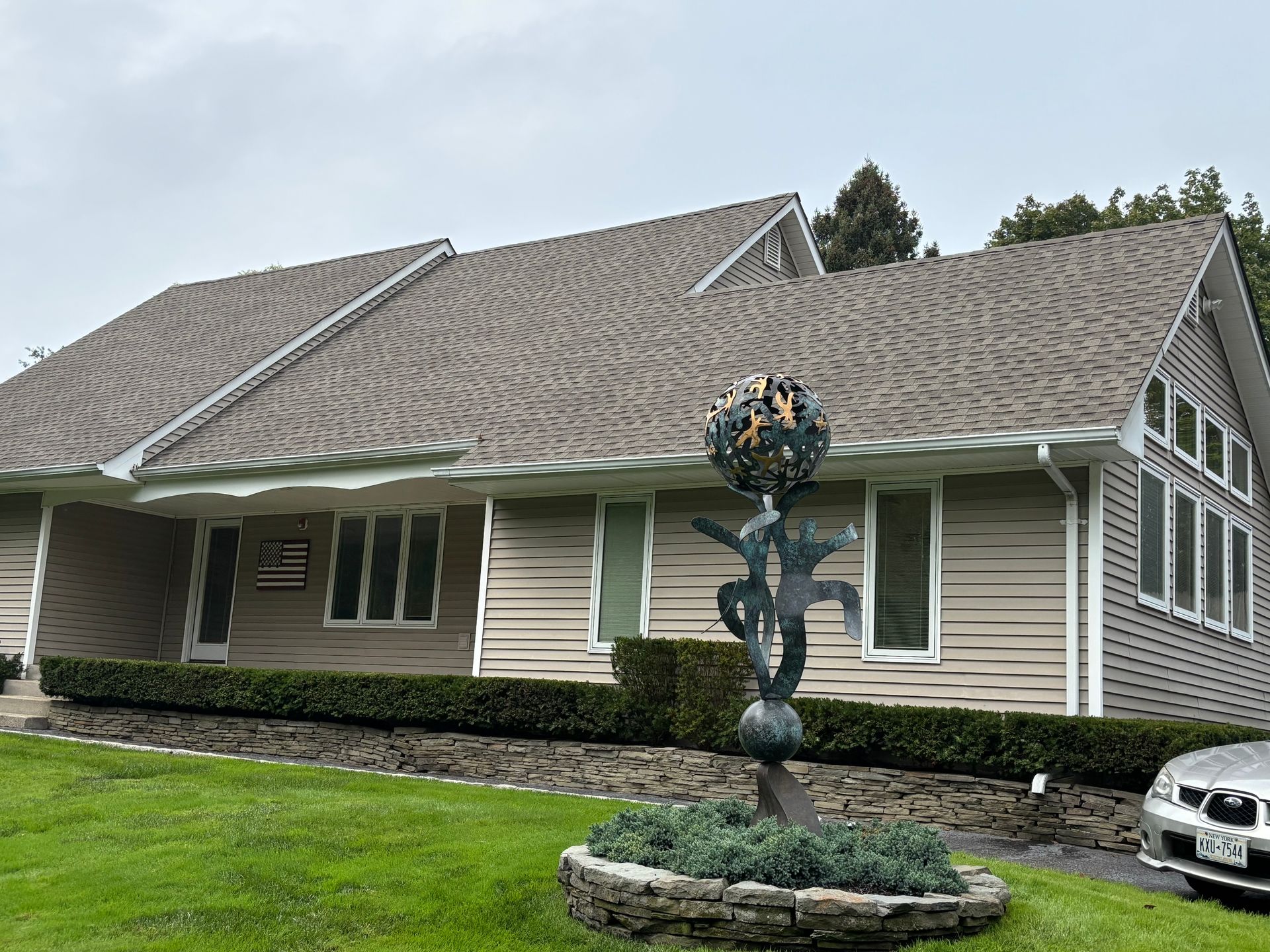 Tan building with a dark roof and sculptural metal art in front.