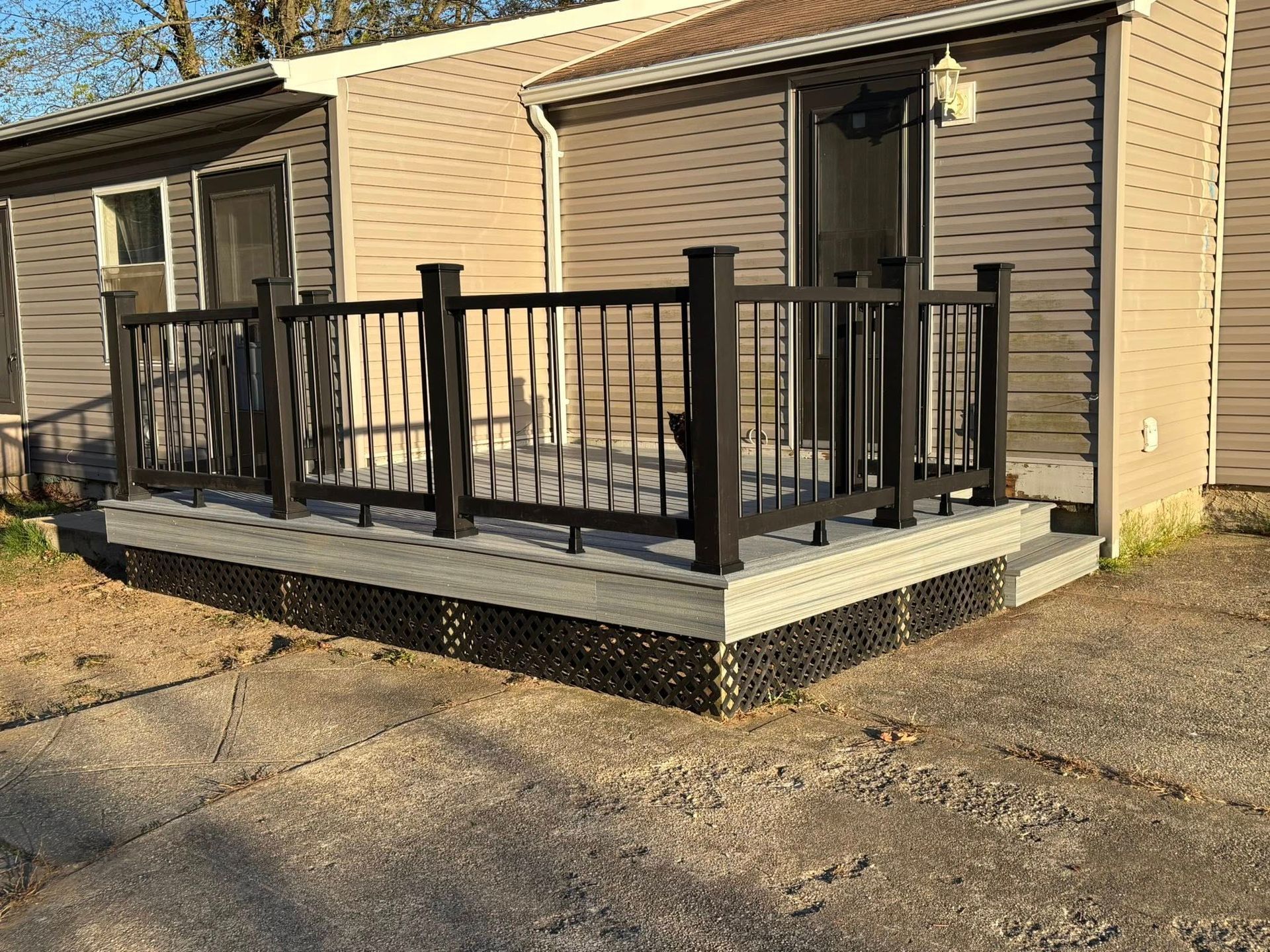 Tan house with a small raised porch and black metal railing beside a gravel driveway.