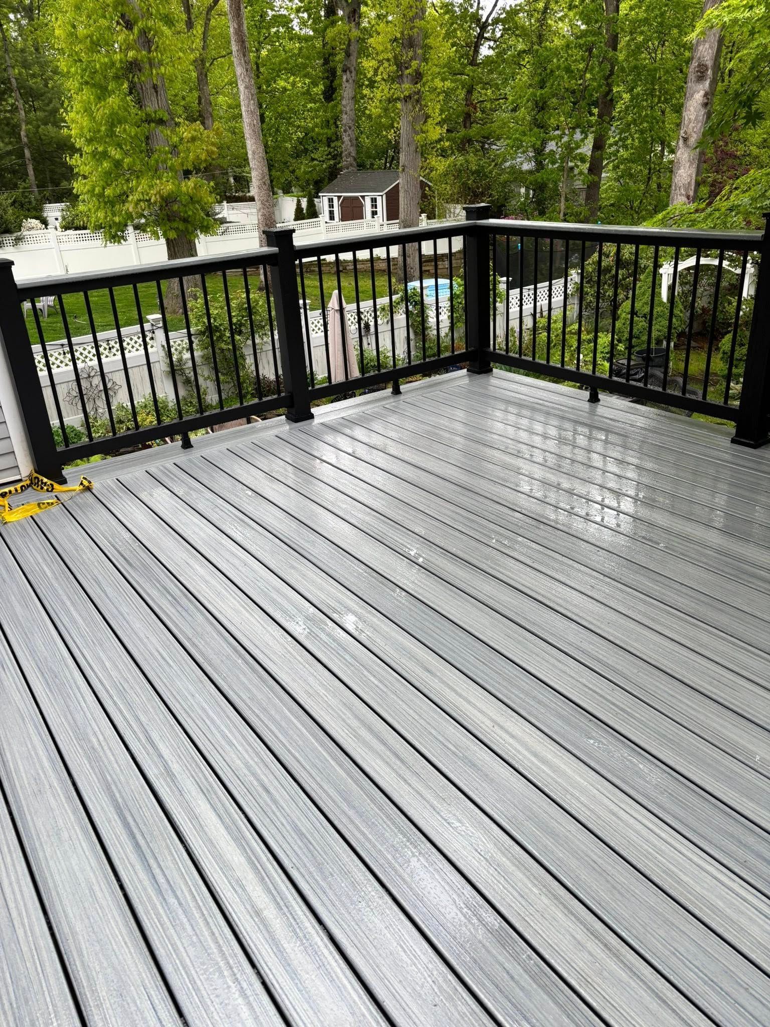 Gray deck with black railing overlooking a tree-lined street and parked cars