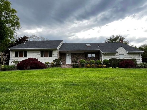 Suburban house with dark roof, white siding, and a large green lawn under cloudy skies