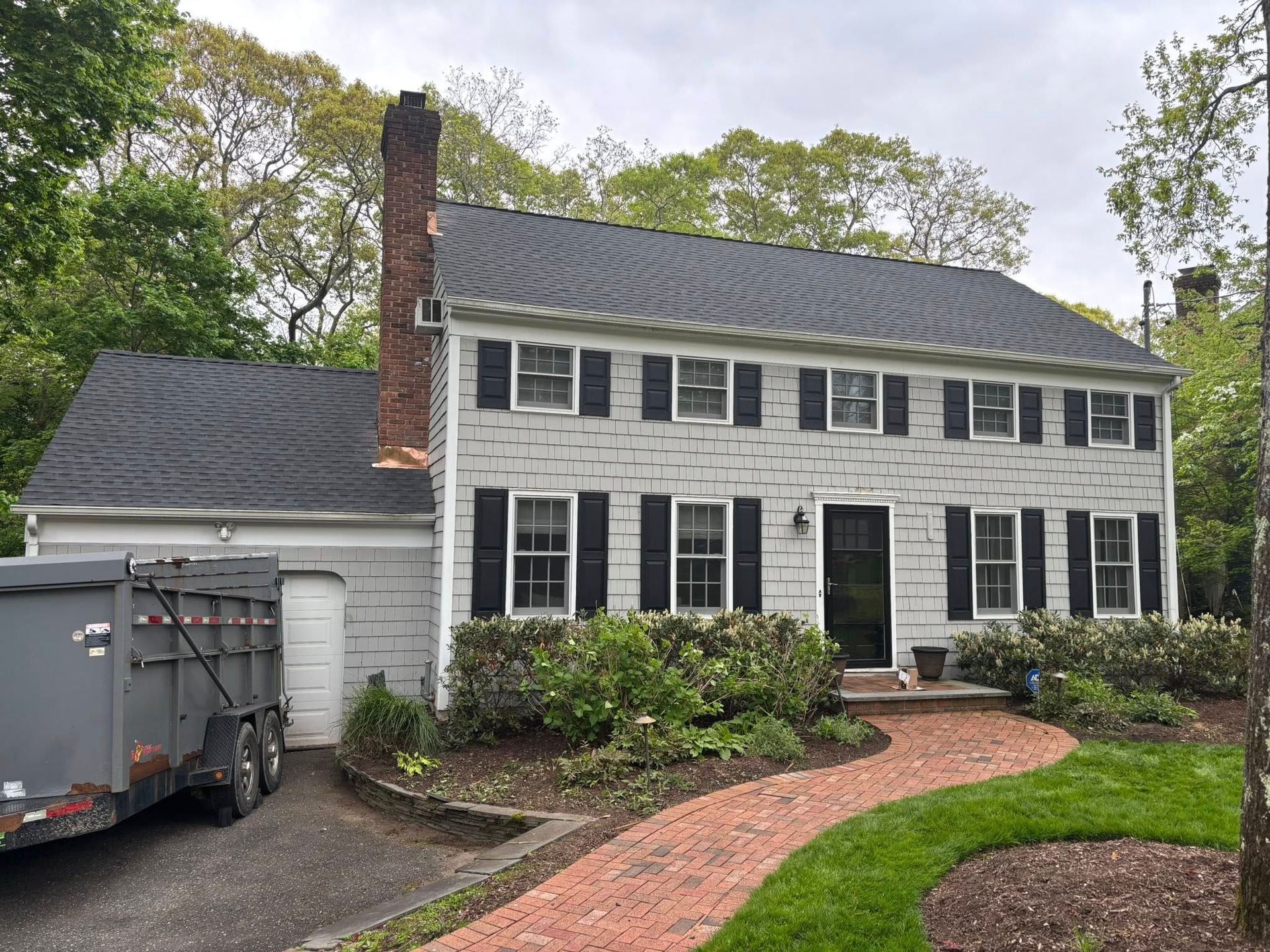 Two-story white colonial house with black shutters, brick walkway, and a trailer in the driveway