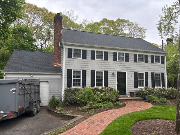 Two-story white colonial house with black shutters, brick walkway, and trailer in driveway