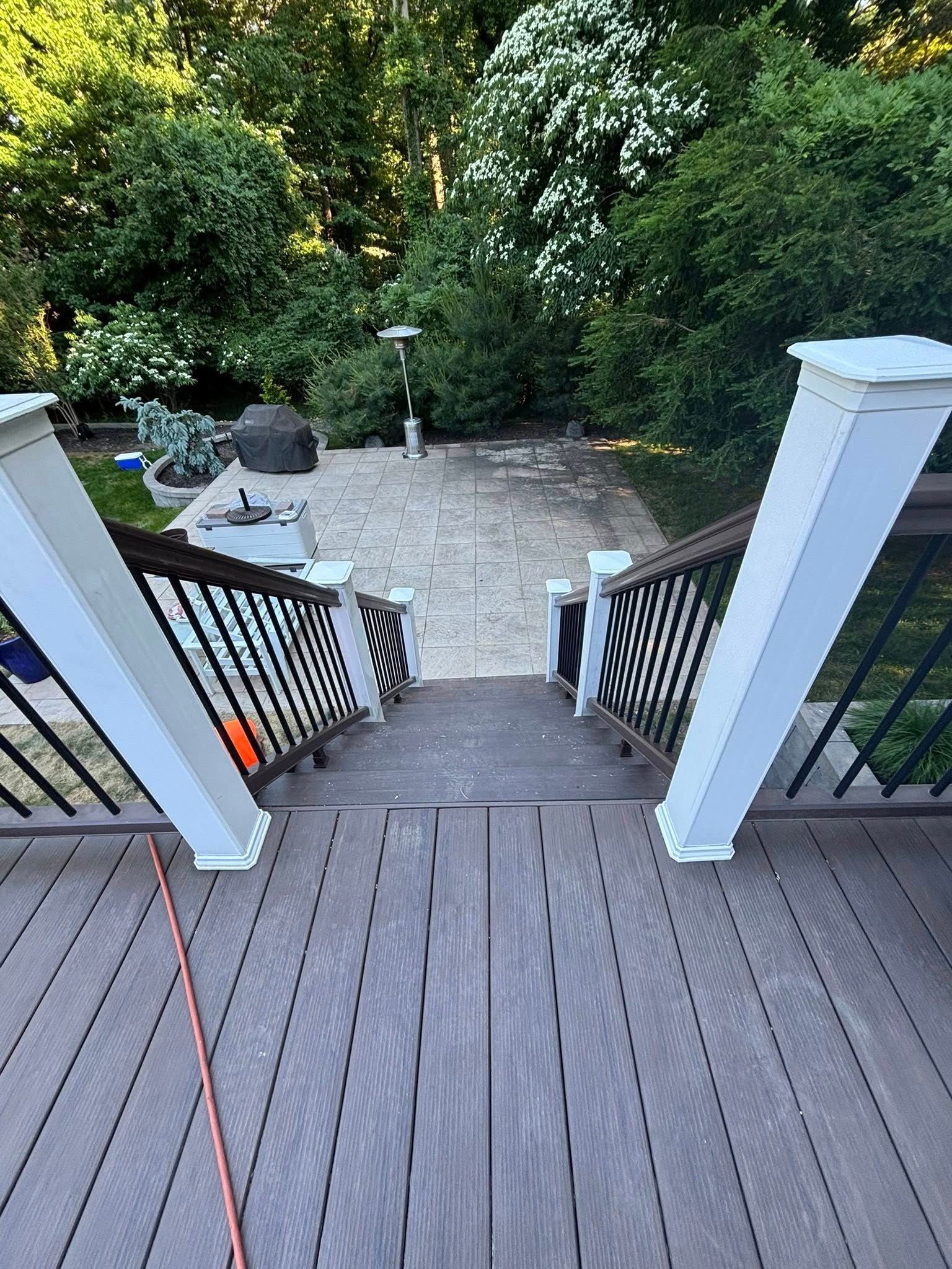 Backyard deck stairs leading to a gravel patio surrounded by dense green trees