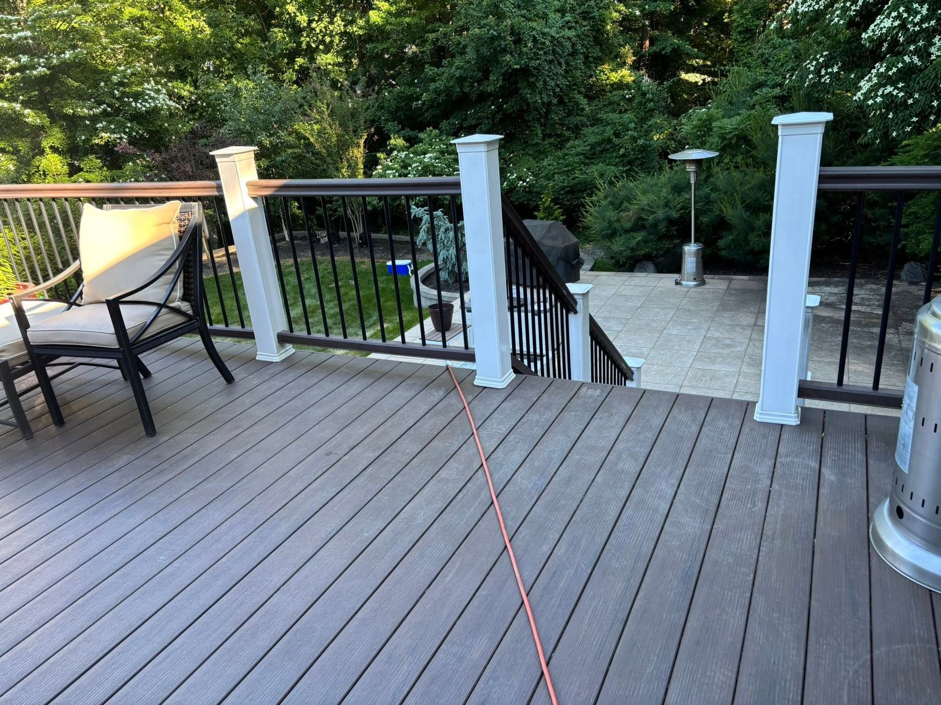 Back deck with white posts, black railings, patio chairs, and an orange extension cord across the floor