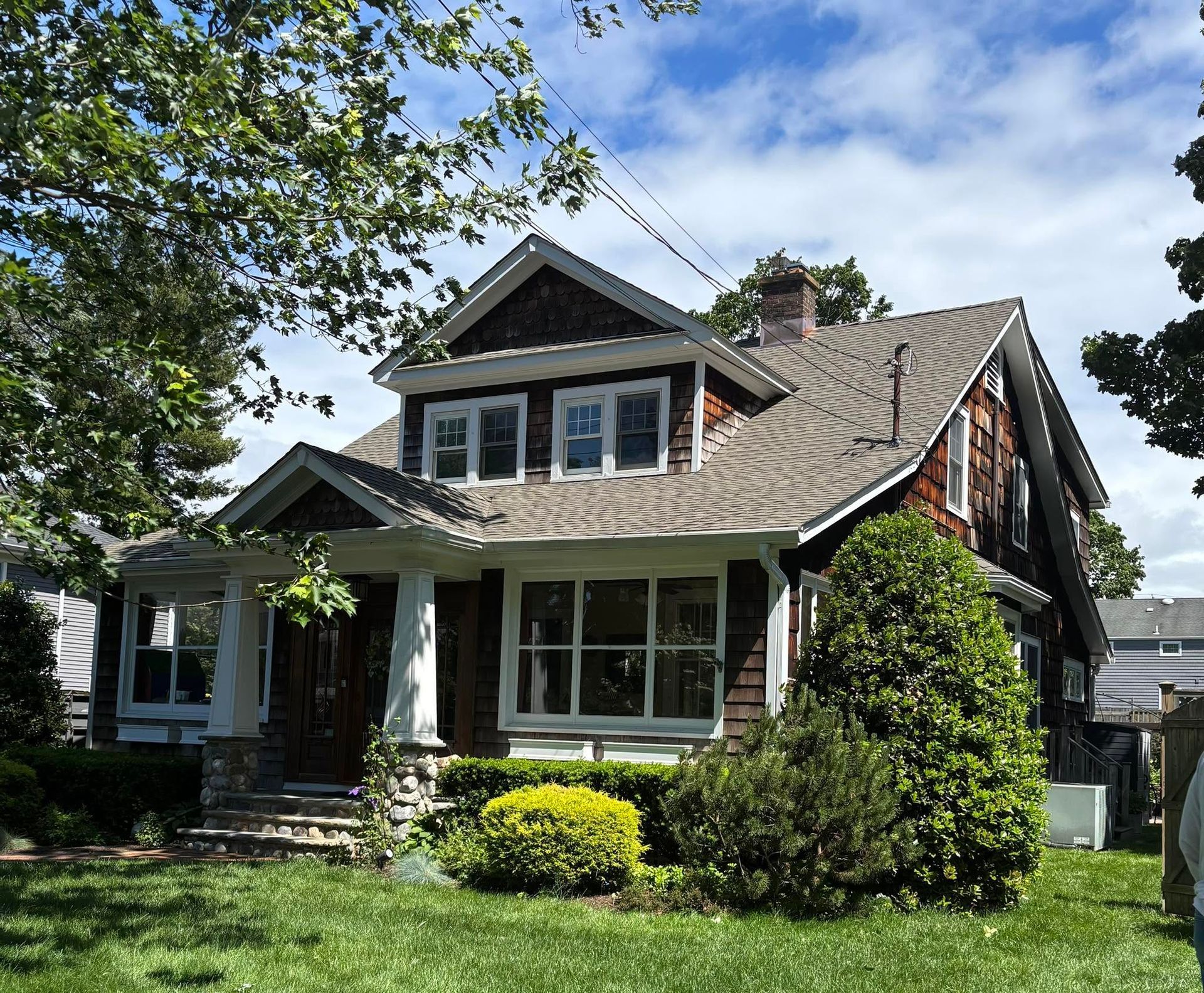 Craftsman-style house with a front porch, green lawn, and trees on a sunny day