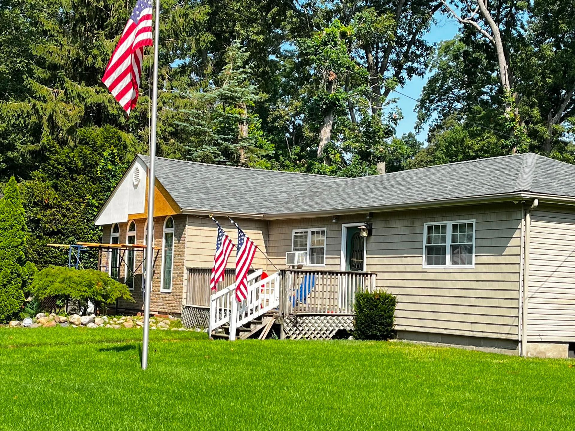 Single-story beige house with American flags and a small front porch, set in a grassy yard.