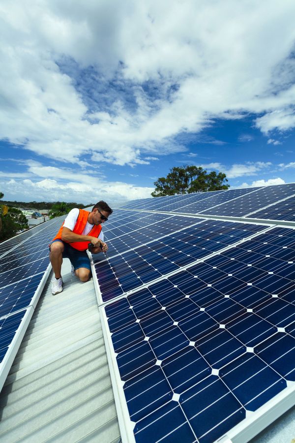 Worker inspecting solar panels on a rooftop under a partly cloudy blue sky