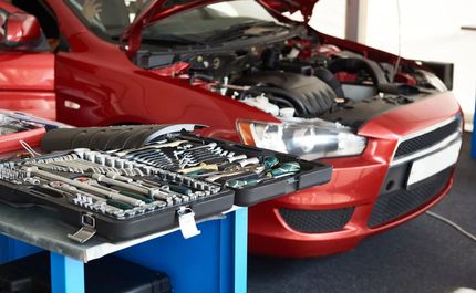 Open car hood with tools on a blue workbench in front of a red car