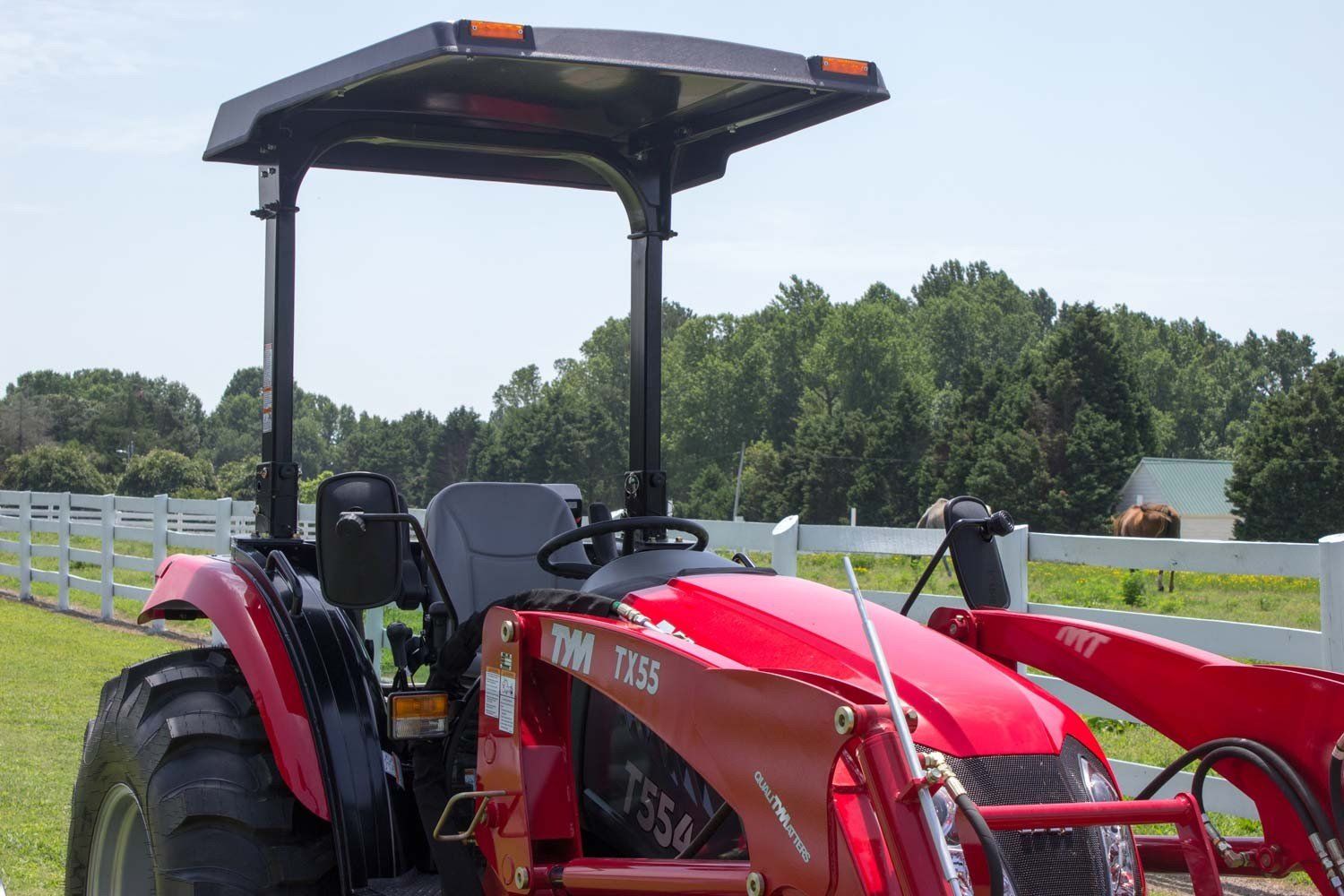 A red tractor is parked in a grassy field next to a white fence.