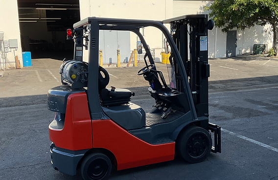 A red and black forklift is parked in a parking lot in front of a building.