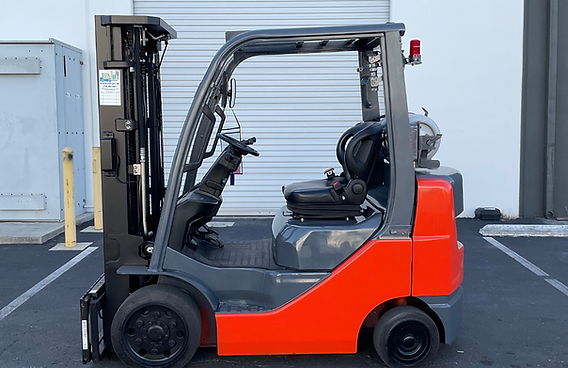 A red and gray forklift is parked in a parking lot in front of a building.