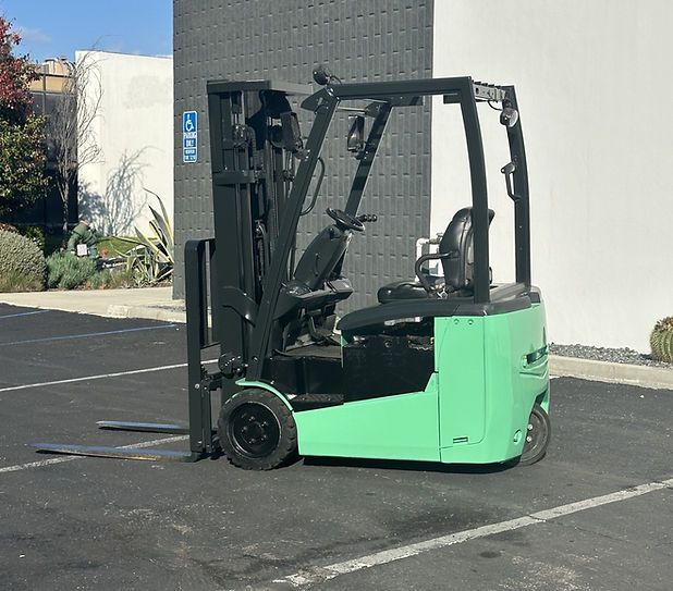 A green forklift is parked in a parking lot in front of a building.