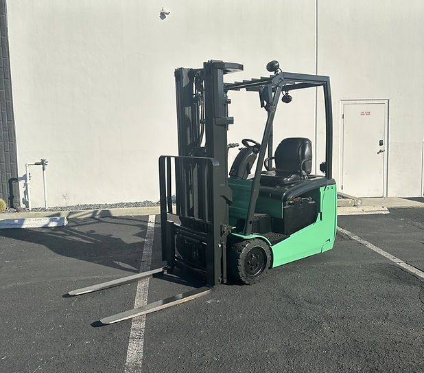 A green forklift is parked in a parking lot in front of a white building.