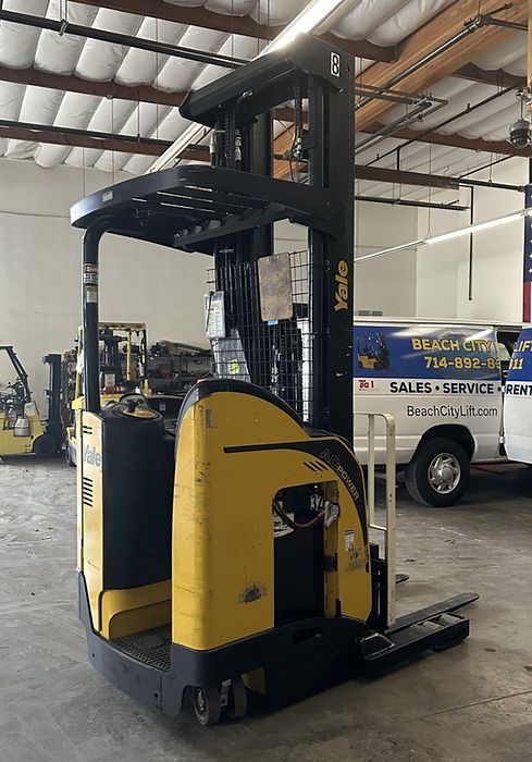 A yellow forklift is parked in a garage next to a van.