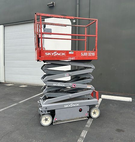 A scissor lift is parked in a parking lot in front of a building.