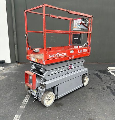 A red and gray scissor lift is parked in a parking lot.