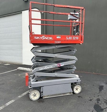 A red scissor lift is parked in a parking lot in front of a building.