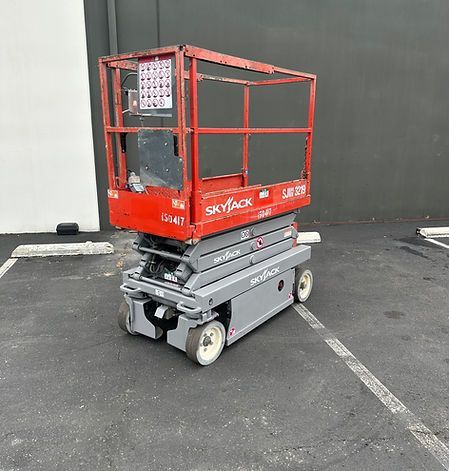 A red and gray scissor lift is parked in a parking lot.