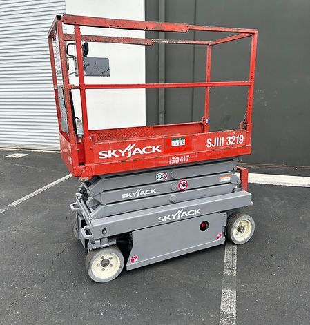 A red and gray scissor lift is parked in a parking lot.